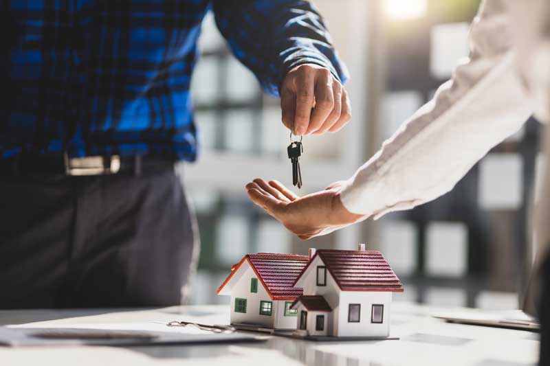 A man hands a key to a woman, who holds a house model, symbolizing home ownership with Millcreek Lighthouse solutions.