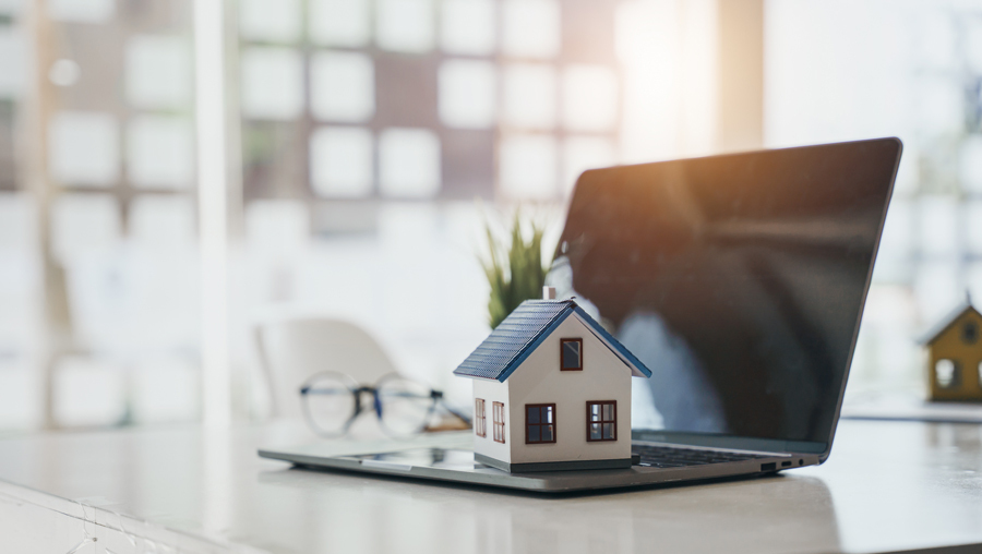 A laptop sits on a table beside a house model, representing Murray's lighthouse home selling solution.