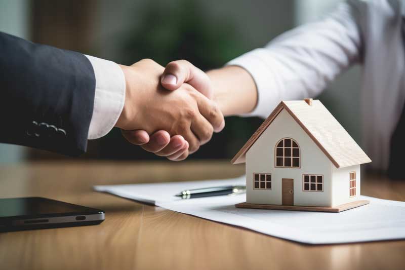 Two individuals shaking hands over a house model, symbolizing a successful real estate transaction in Ogden's Lighthouse Home Selling Solution.