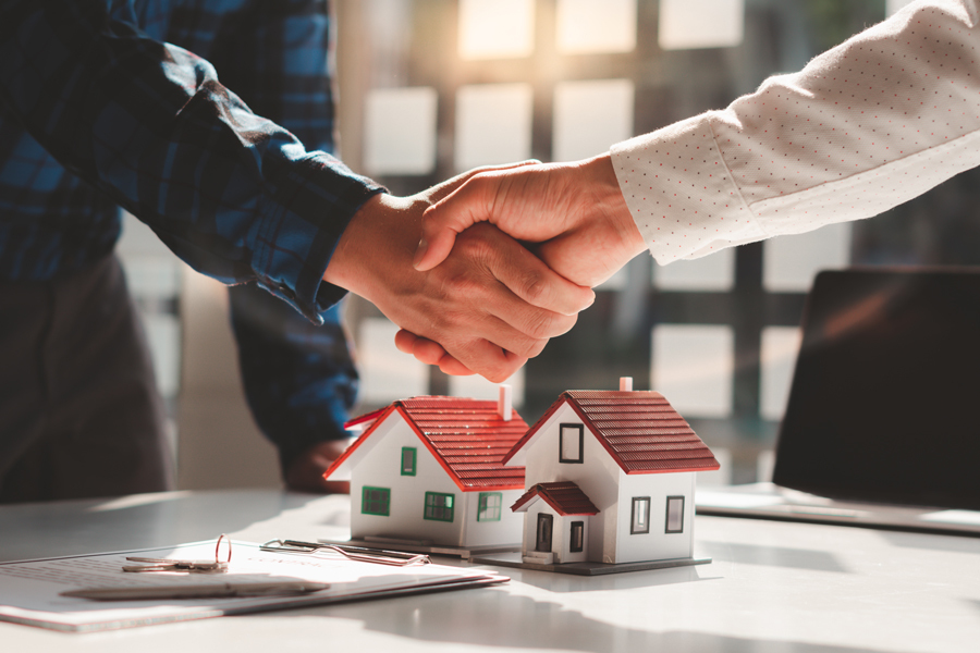 Two individuals shaking hands above a house model, symbolizing a successful real estate transaction in Provo.