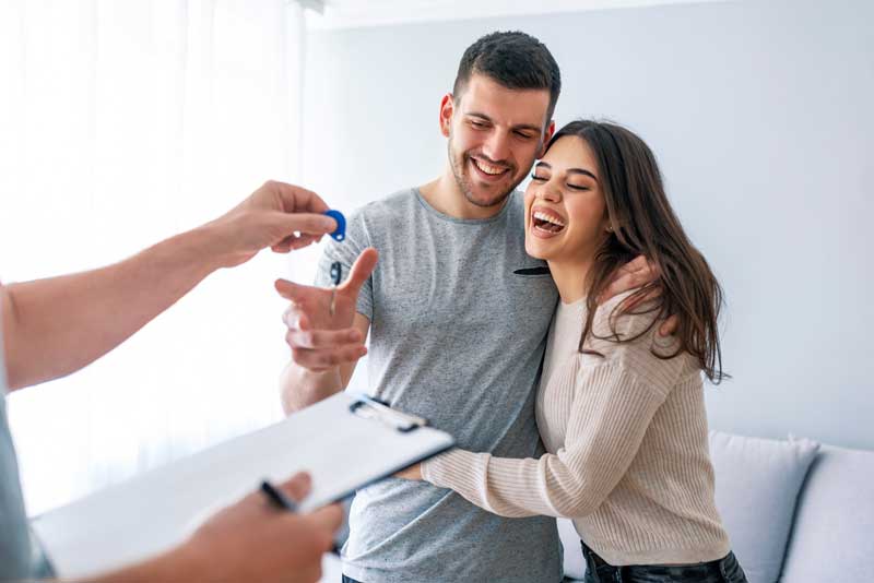 A smiling couple in Salt Lake City proudly holds a house key, celebrating their new home with Lighthouse Home Selling Solution.