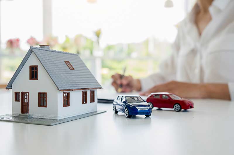 A woman uses a pen to write on paper, with a house model nearby, illustrating West Valley's lighthouse home selling service.